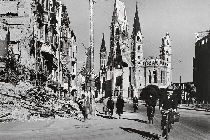 Menschen entlang einer von zerstörten Gebäuden gesäumten Straße