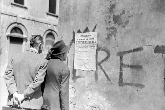 Des passants lisent le titre de la deuxième édition du journal Milano-Sera affiché sur un mur
