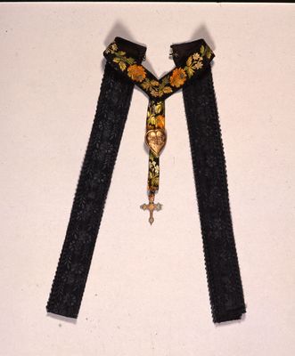 Croix décorée d'or attachée avec un ruban brodé et un coeur gravé